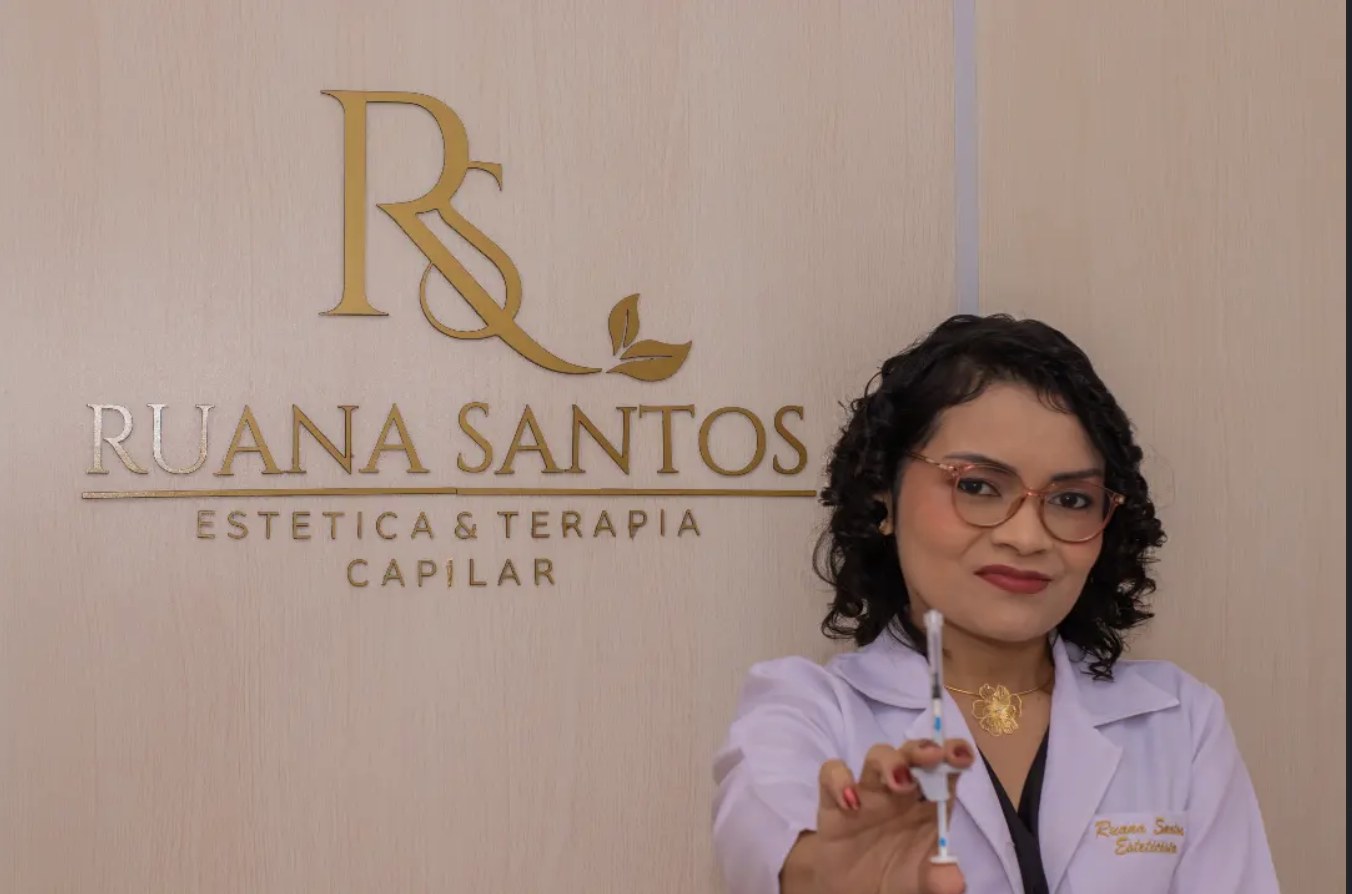 Ruana Santos na clínica, ao lado do logo dourado Estética e Terapia Capilar